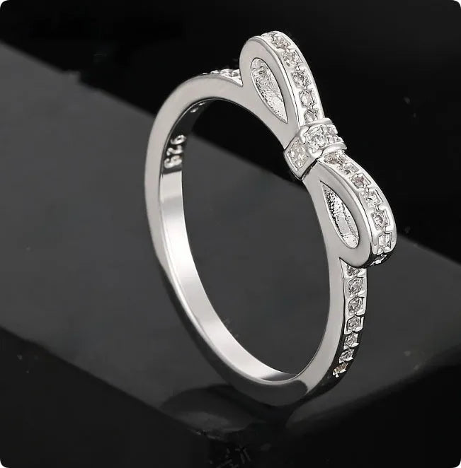 Silver couple ring with a bow-shaped centre decorated with sparkling rhinestone crystals on a finger.