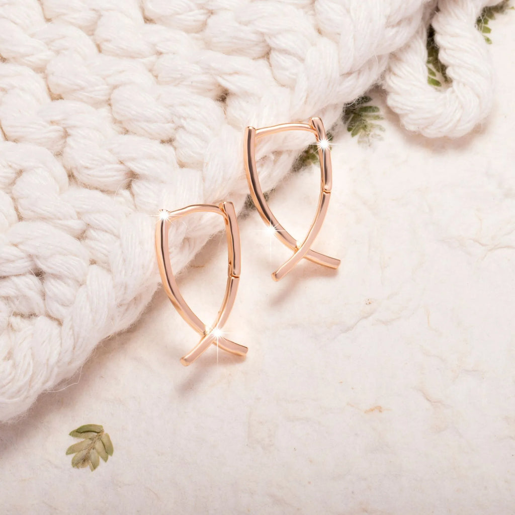 A pair of rose gold coloured cross-shaped stud earrings on a plain background.