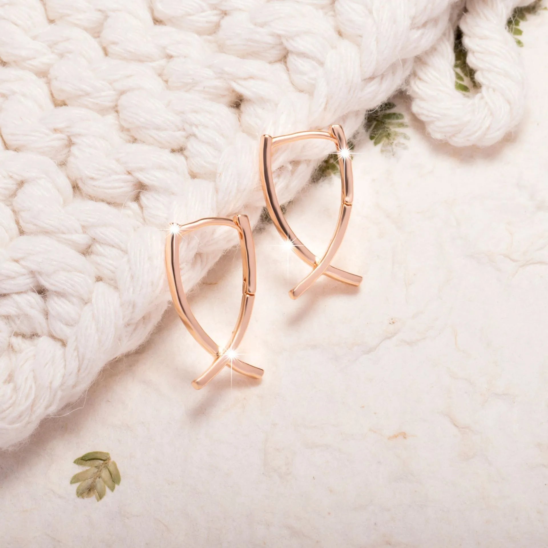 A pair of rose gold coloured cross-shaped stud earrings on a plain background.