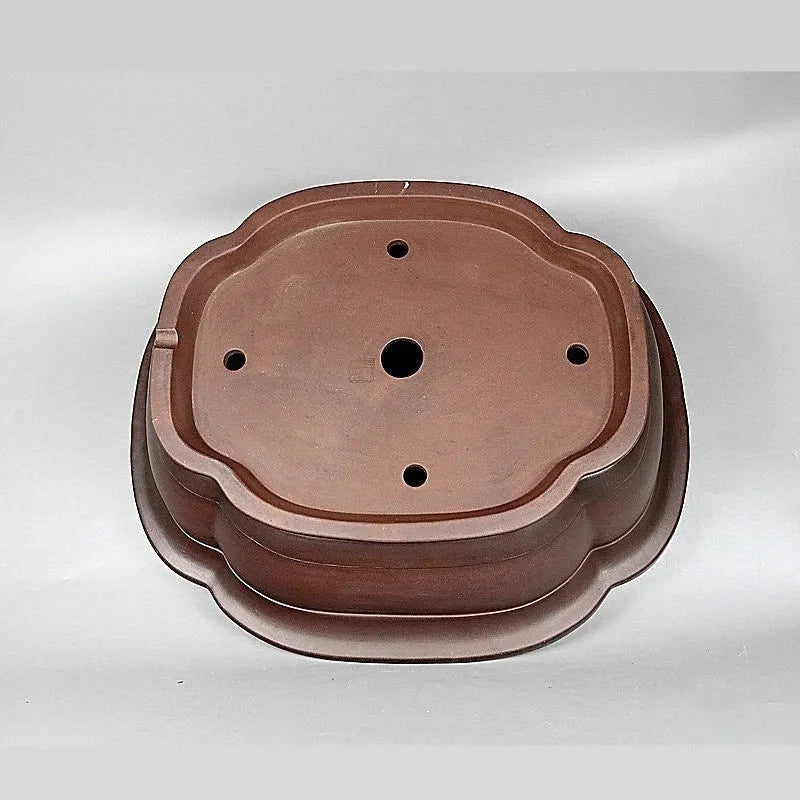 Handmade antique crabapple shaped purple clay flower pot on a wooden floor.