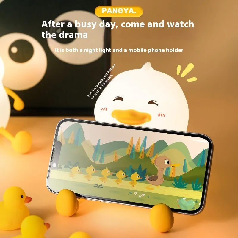 Chubby white silicone rechargeable night light on a wooden desk, showing phone holder function.