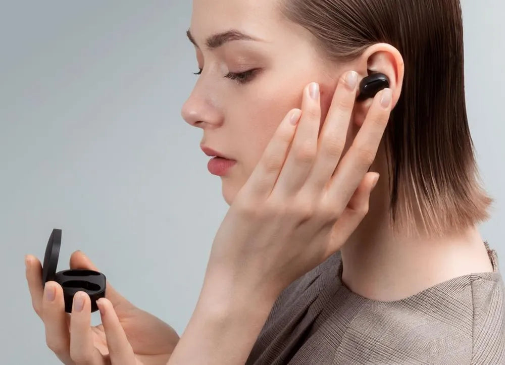 Redmi AirDots black true wireless earbuds next to their compact white charging case.