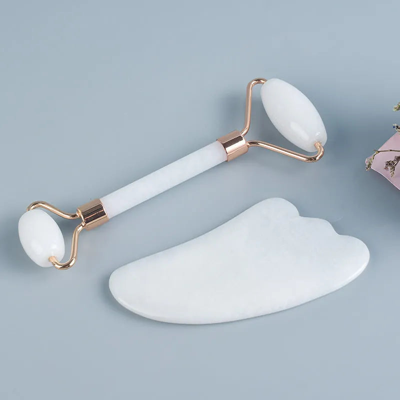 White jade facial roller set with double-headed roller, claw tool, and gua sha board on a wooden table.
