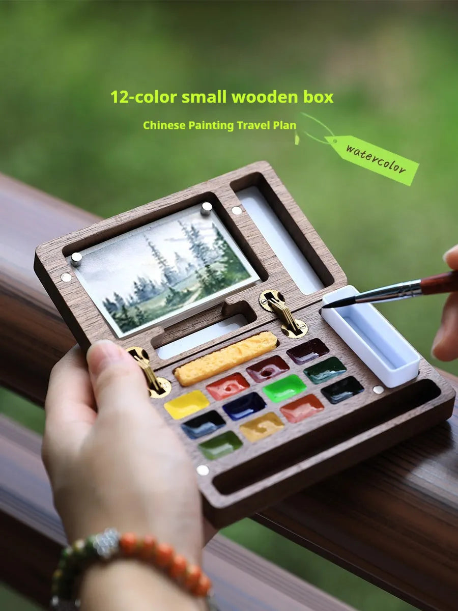 Mini wooden watercolour paint box open showing professional pigment compartments with carrying handle
