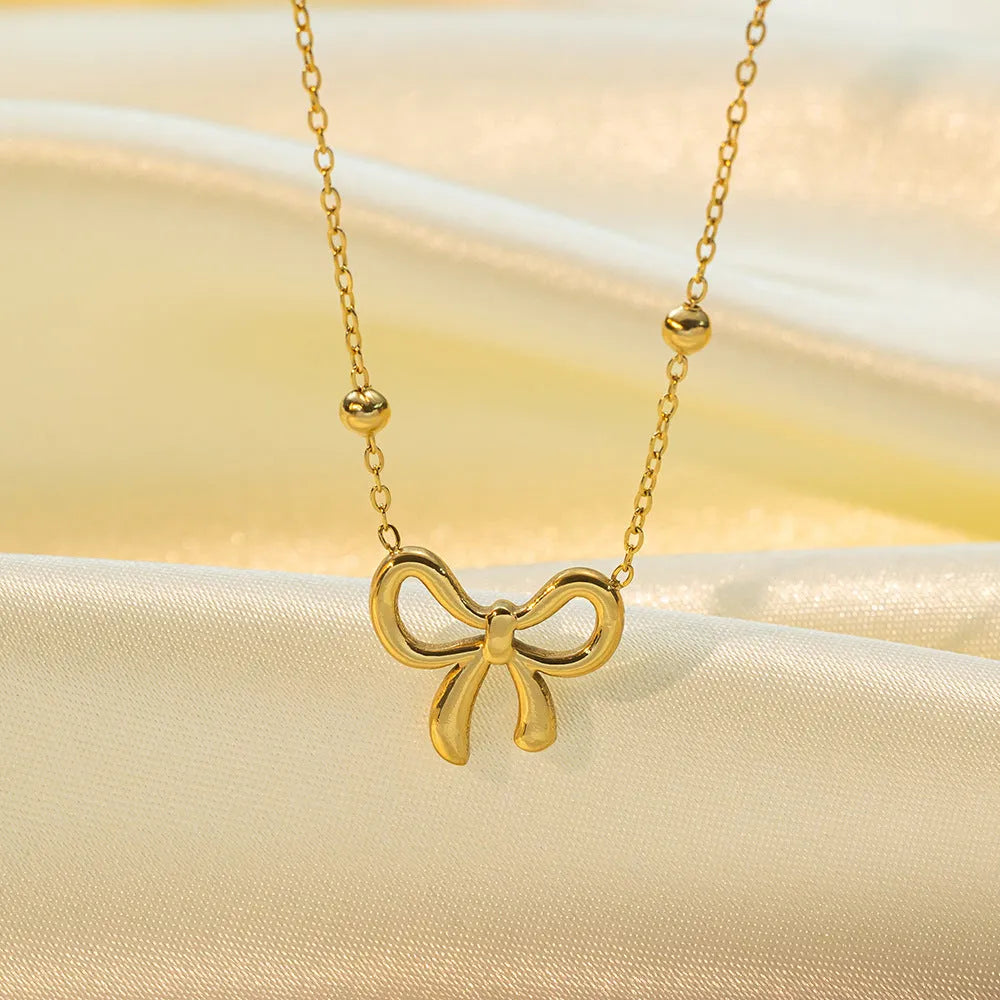 Gold electroplated women's bow necklace with cross chain design on white background
