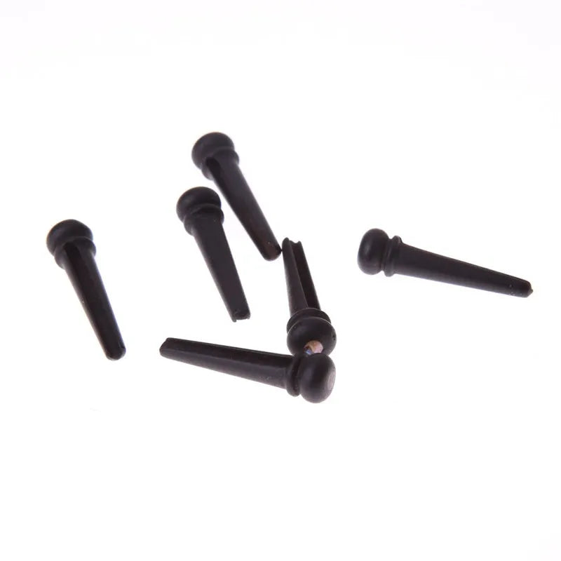 Six matt black ebony folk guitar string nails on a grey background