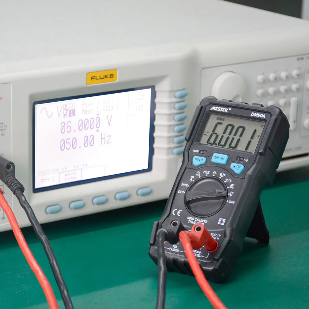 DM90A digital multimeter with test leads on a workbench, showing its large display and rotary function selector.