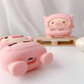 Pink silicone AirPods case with cartoon pig in sweater design, shown with flip lid open and a matching metal hook.