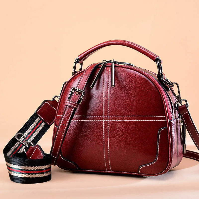 Round leather handbag with zipper opening and soft handle in wine red colour
