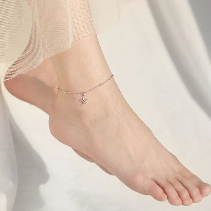 Close-up of a sterling silver anklet with a small starfish charm on a woman's ankle.