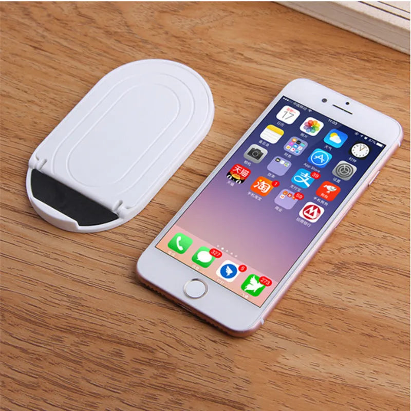 Adjustable plastic mobile phone stand in multiple colours on a table, holding a smartphone at an angle