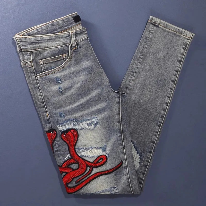 Man wearing slim fit distressed blue jeans with hole patches and embroidered details on the legs.