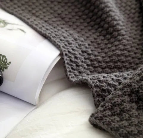 Nordic-style fringed knit acrylic blanket in a plain pattern, shown in a neutral colour on a sofa.