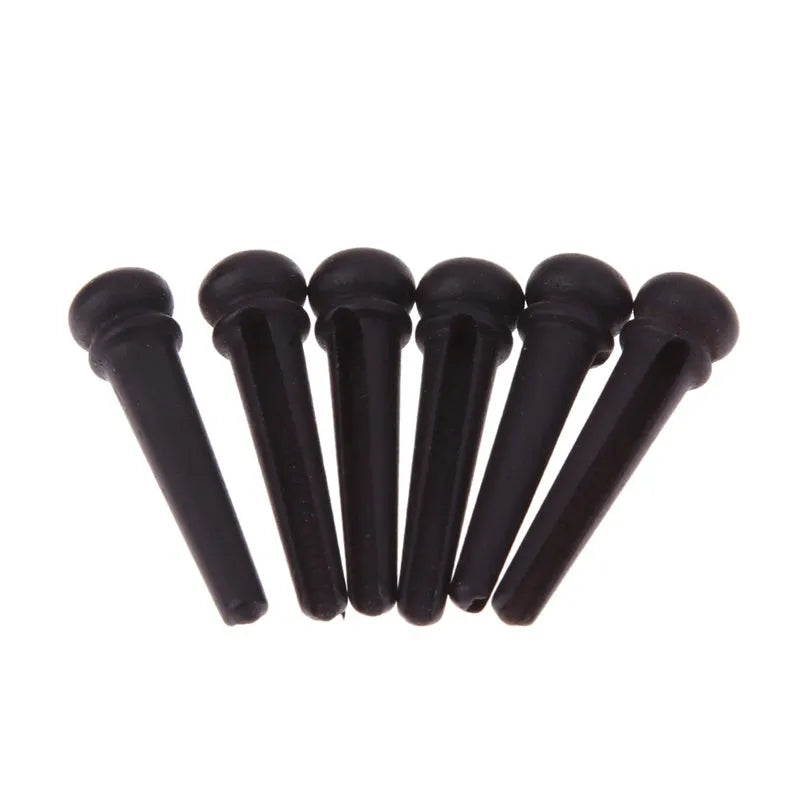 Six matt black ebony folk guitar string nails on a grey background