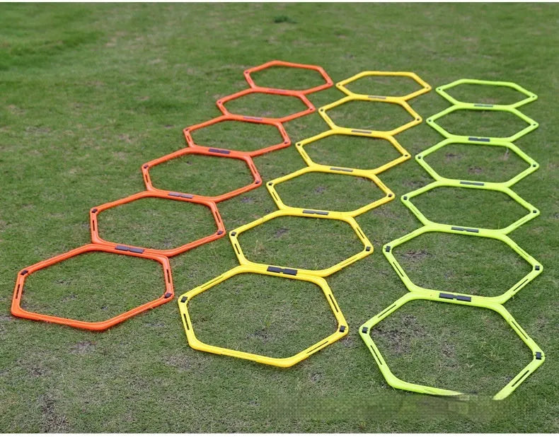 Set of six bright green, orange, and yellow foldable hexagon football agility training rings laid out on grass.