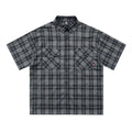 Man wearing a black loose-fit plaid short sleeve shirt with embroidered lettering on the chest.