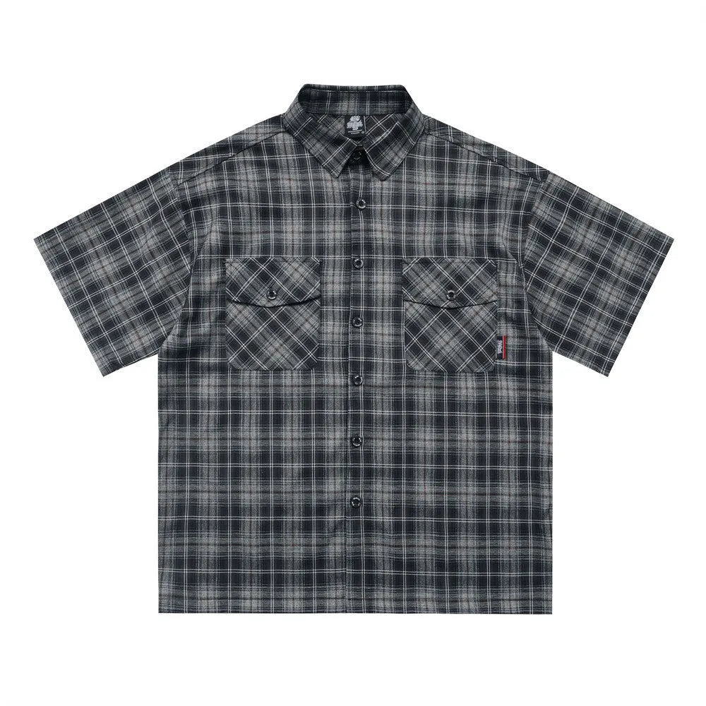 Man wearing a black loose-fit plaid short sleeve shirt with embroidered lettering on the chest.