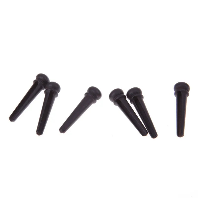Six matt black ebony folk guitar string nails on a grey background