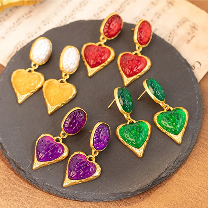 Close-up of a pair of textured needle-pleated oval heart stud earrings in an alloy metal, showing colour options.