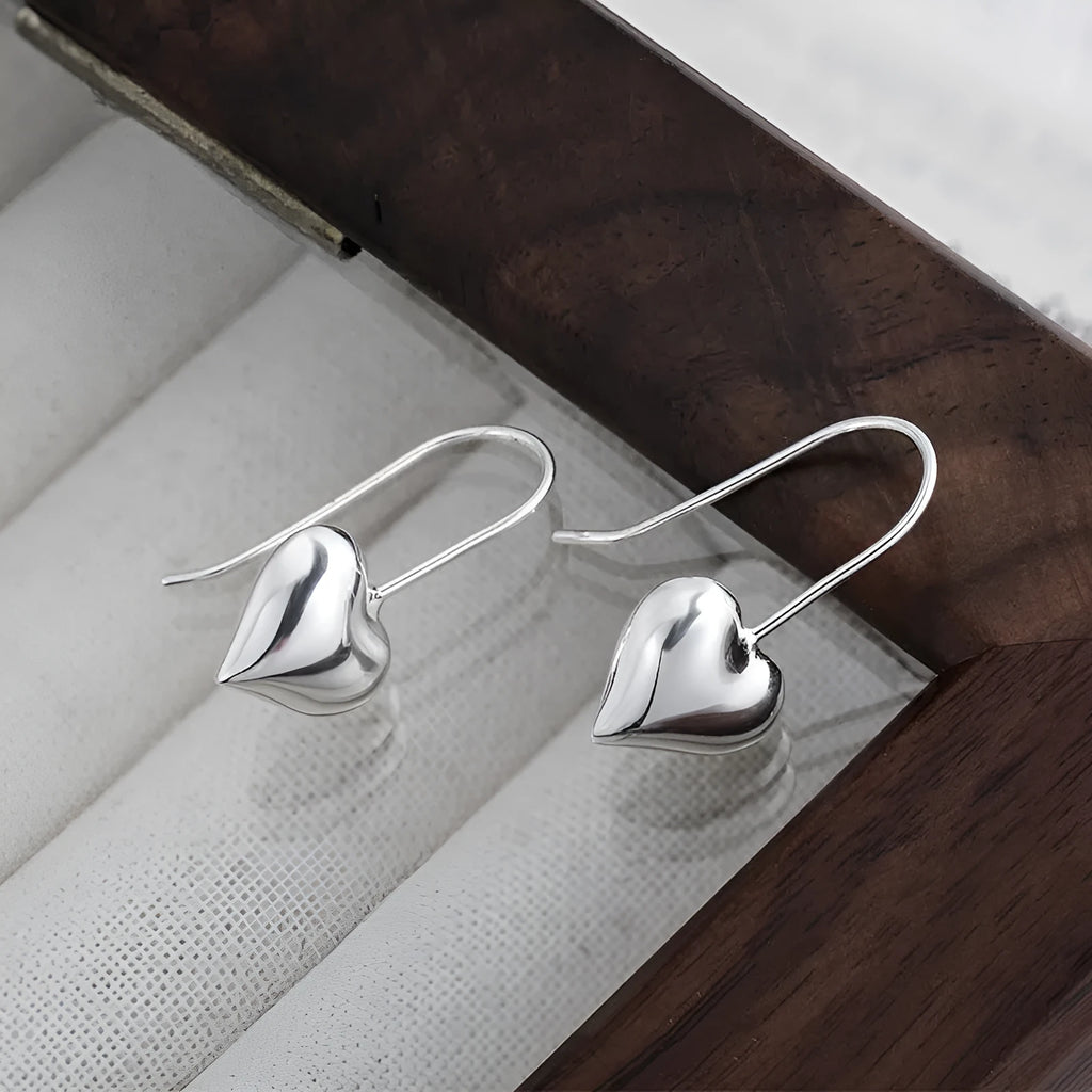 Silver-toned heart-shaped women's earrings with glossy finish and matching heart-shaped ear hooks.