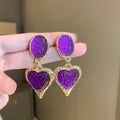 Close-up of a pair of textured needle-pleated oval heart stud earrings in an alloy metal, showing colour options.