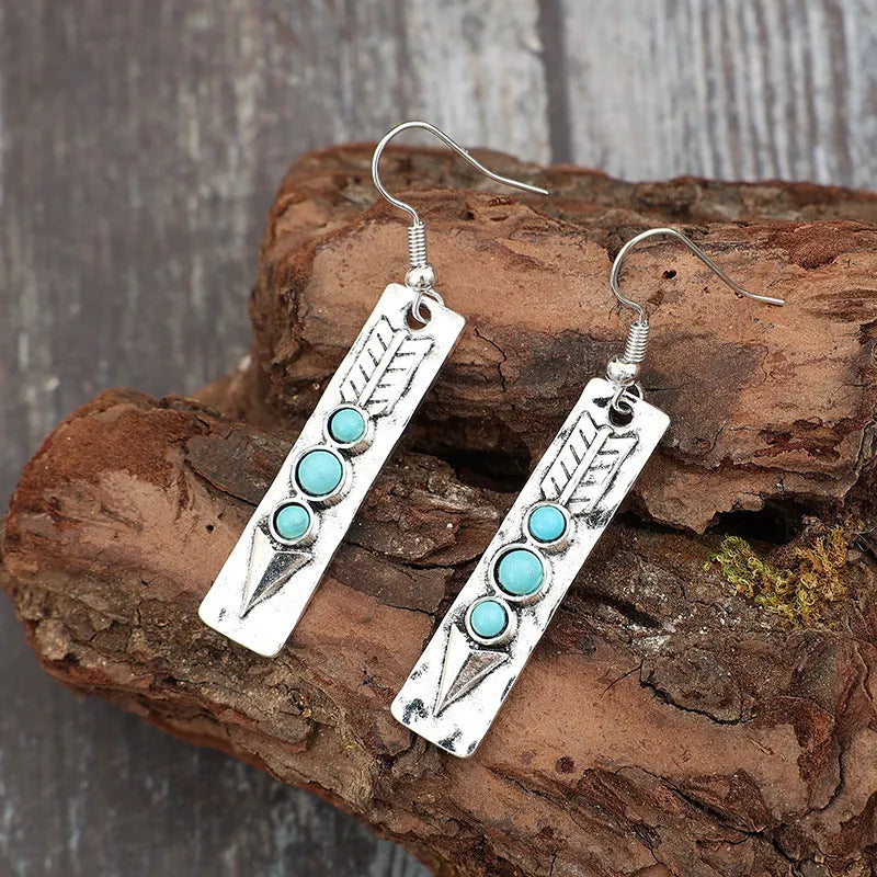 Long silver geometric earrings with a blue turquoise stone detail on a white background.
