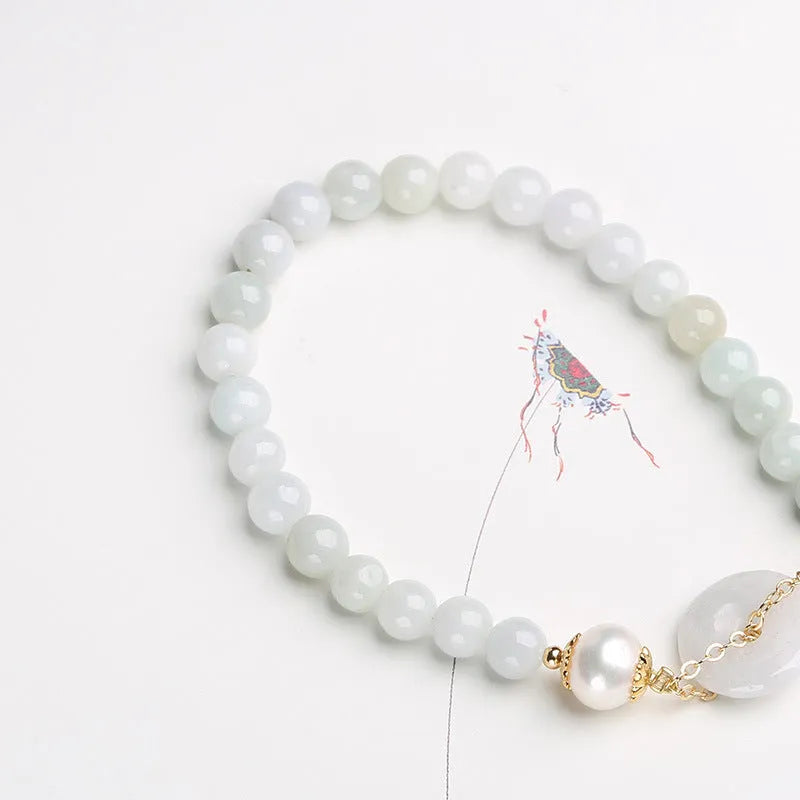 Close-up of a women's bracelet with a jade peace symbol buckle on a string of freshwater pearls.