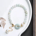 Close-up of a women's bracelet with a jade peace symbol buckle on a string of freshwater pearls.
