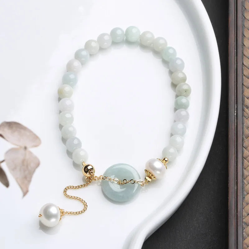 Close-up of a women's bracelet with a jade peace symbol buckle on a string of freshwater pearls.