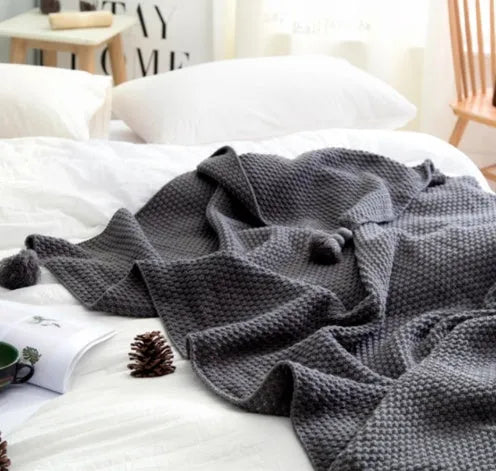 Nordic-style fringed knit acrylic blanket in a plain pattern, shown in a neutral colour on a sofa.