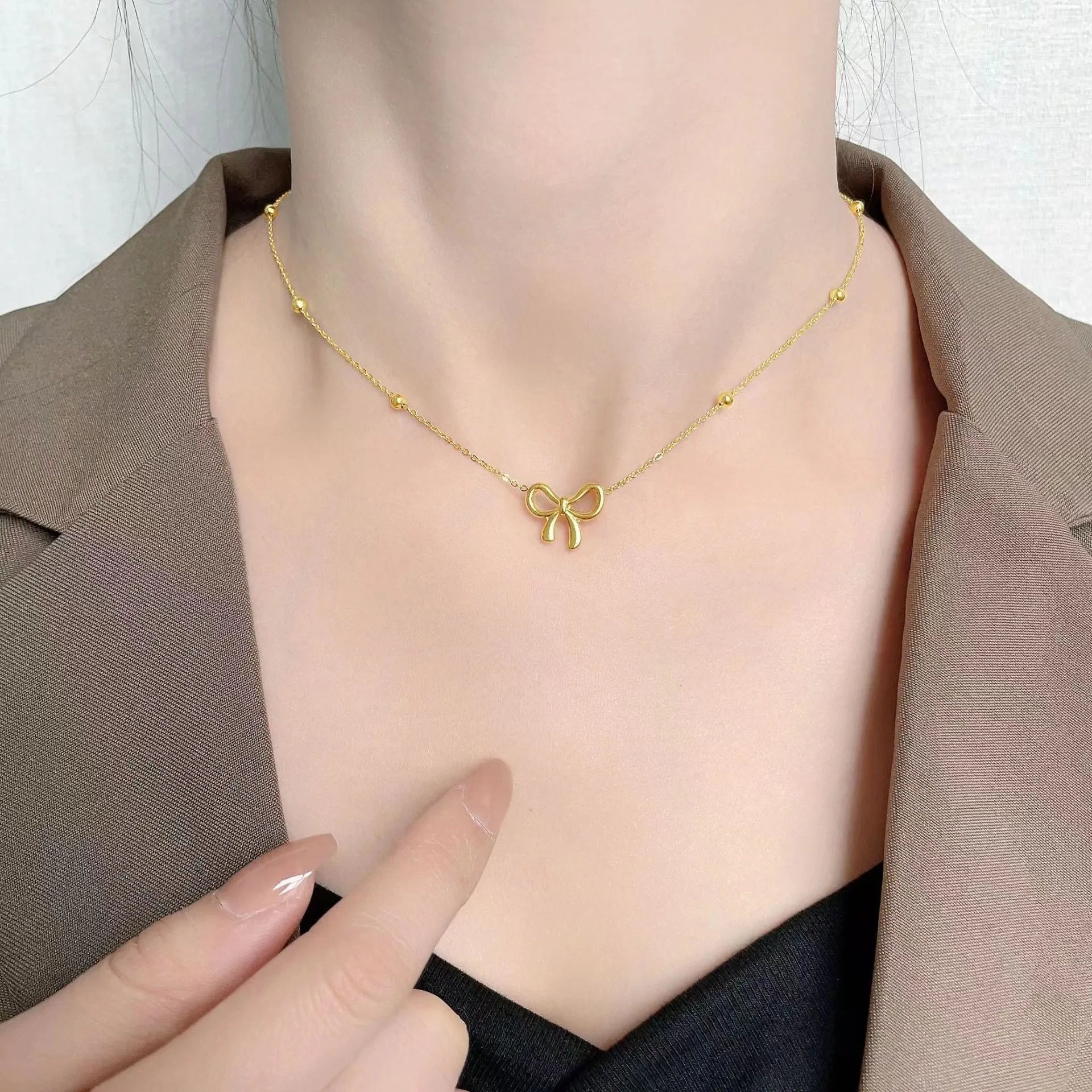 Gold electroplated women's bow necklace with cross chain design on white background