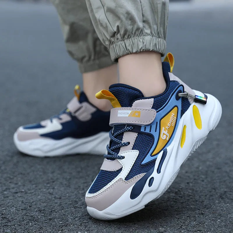 Boys sports running shoes in dark blue with a mesh upper and Velcro strap, shown on a hard ground surface.