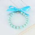 Small dog wearing a blue imitation pearl and rhinestone necklace with a ribbon bow.