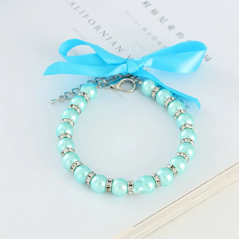 Small dog wearing a blue imitation pearl and rhinestone necklace with a ribbon bow.