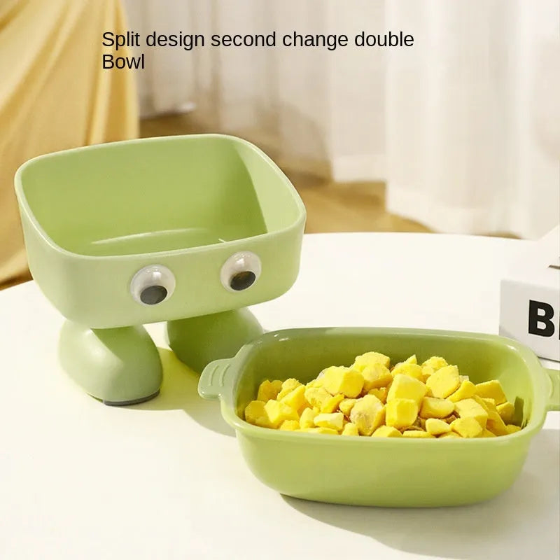 Green cartoon robot-shaped elevated cat bowl with tilted design and non-slip base on a table.