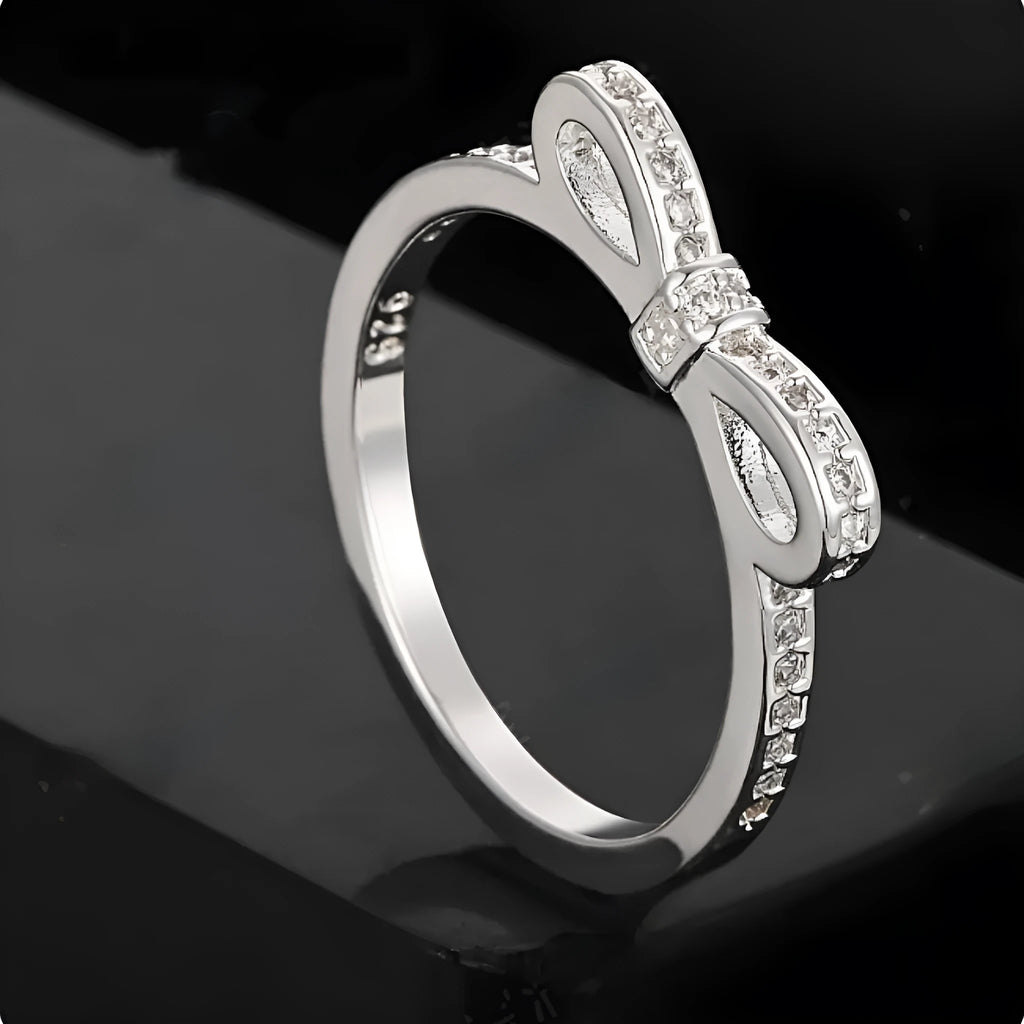 Silver couple ring with a bow-shaped centre decorated with sparkling rhinestone crystals on a finger.