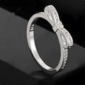 Silver couple ring with a bow-shaped centre decorated with sparkling rhinestone crystals on a finger.