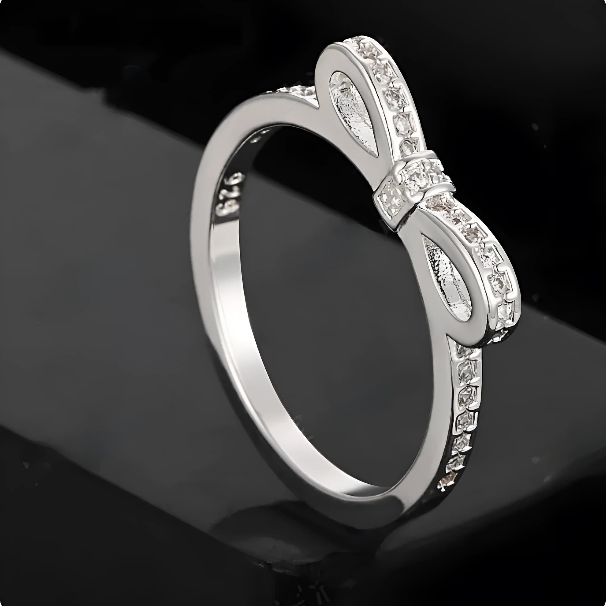 Silver couple ring with a bow-shaped centre decorated with sparkling rhinestone crystals on a finger.