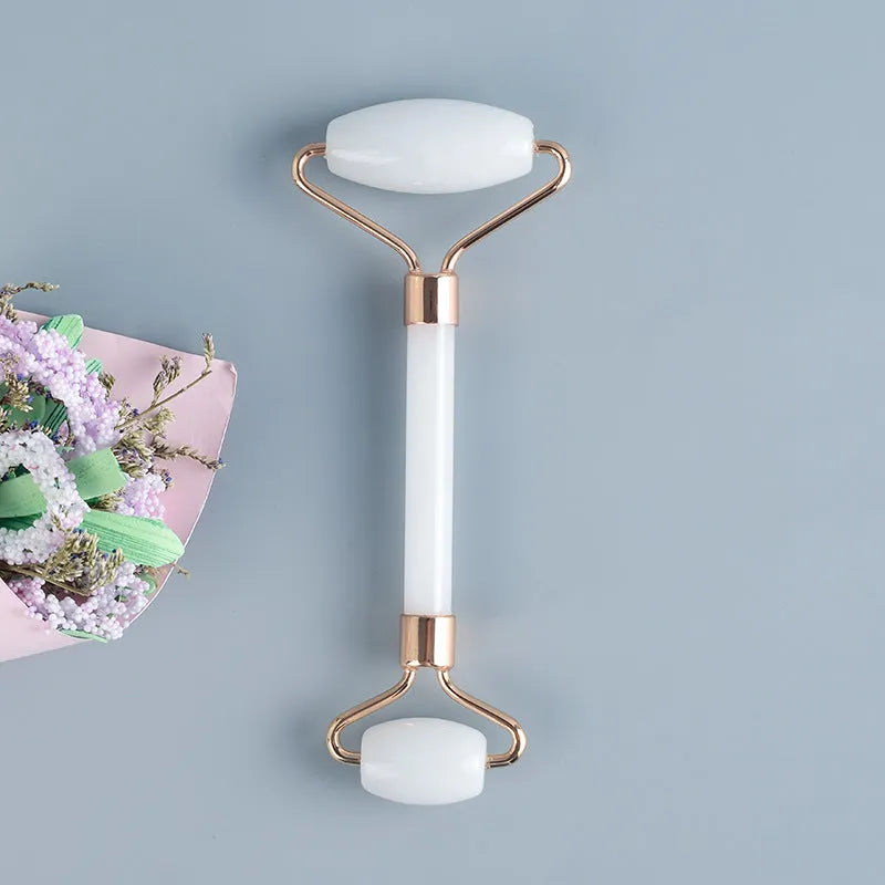 White jade facial roller set with double-headed roller, claw tool, and gua sha board on a wooden table.
