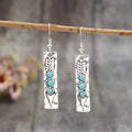 Long silver geometric earrings with a blue turquoise stone detail on a white background.