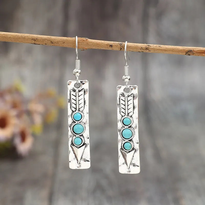 Long silver geometric earrings with a blue turquoise stone detail on a white background.