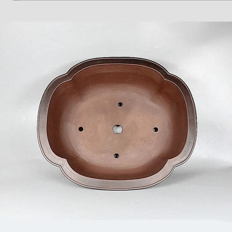 Handmade antique crabapple shaped purple clay flower pot on a wooden floor.