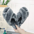 Women's black cross open-toe fur slippers with a patterned non-slip sole on a wooden floor.