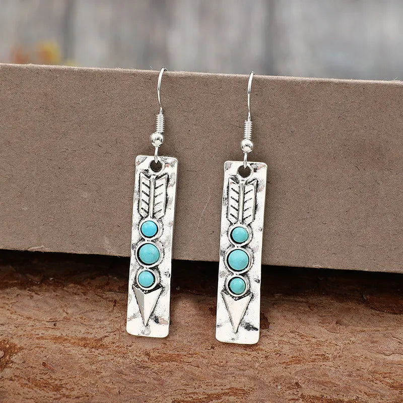 Long silver geometric earrings with a blue turquoise stone detail on a white background.