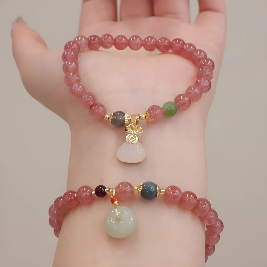 Women's strawberry quartz bracelet with gold purse-shaped safety buckle and lucky bag charm on geometric beads.