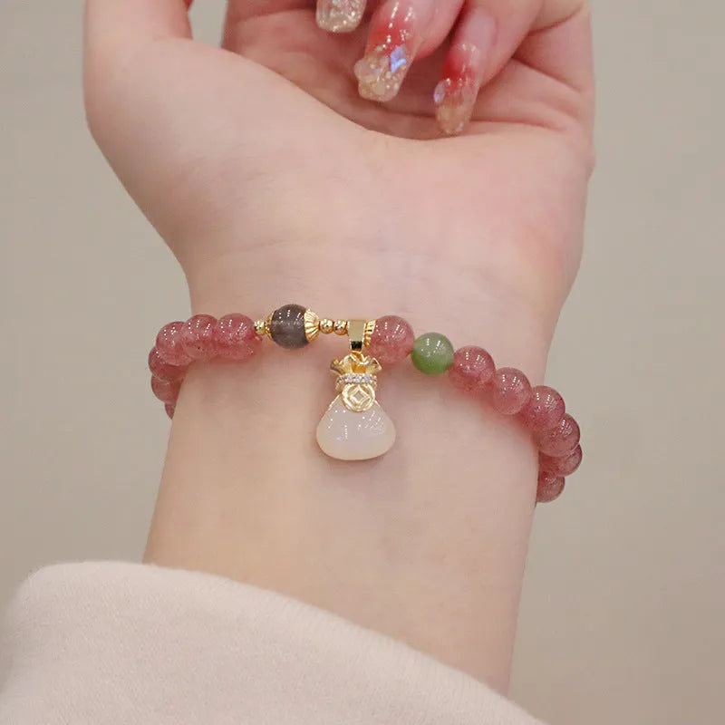 Women's strawberry quartz bracelet with gold purse-shaped safety buckle and lucky bag charm on geometric beads.