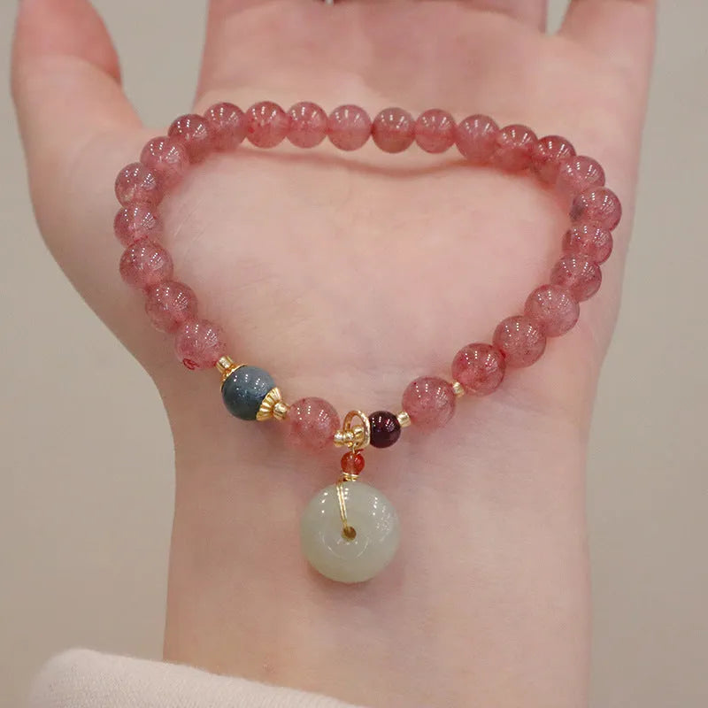 Women's strawberry quartz bracelet with gold purse-shaped safety buckle and lucky bag charm on geometric beads.