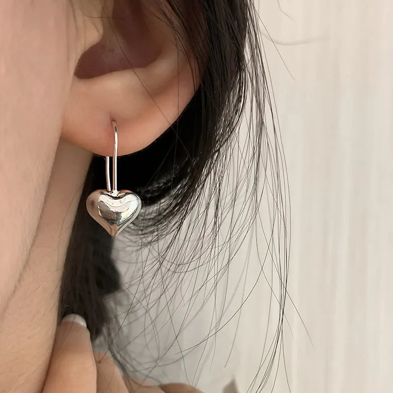 Silver-toned heart-shaped women's earrings with glossy finish and matching heart-shaped ear hooks.