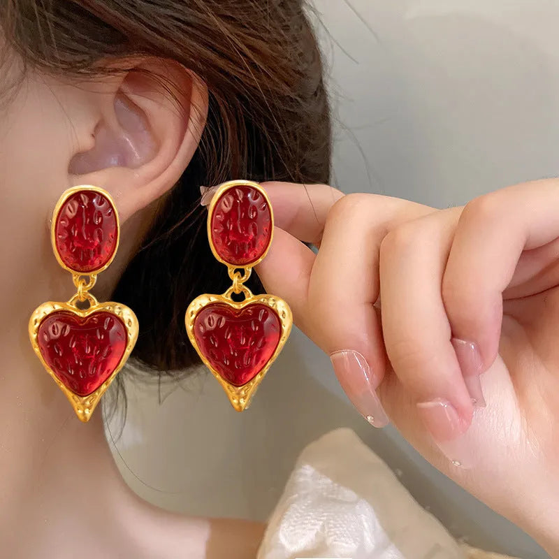 Close-up of a pair of textured needle-pleated oval heart stud earrings in an alloy metal, showing colour options.