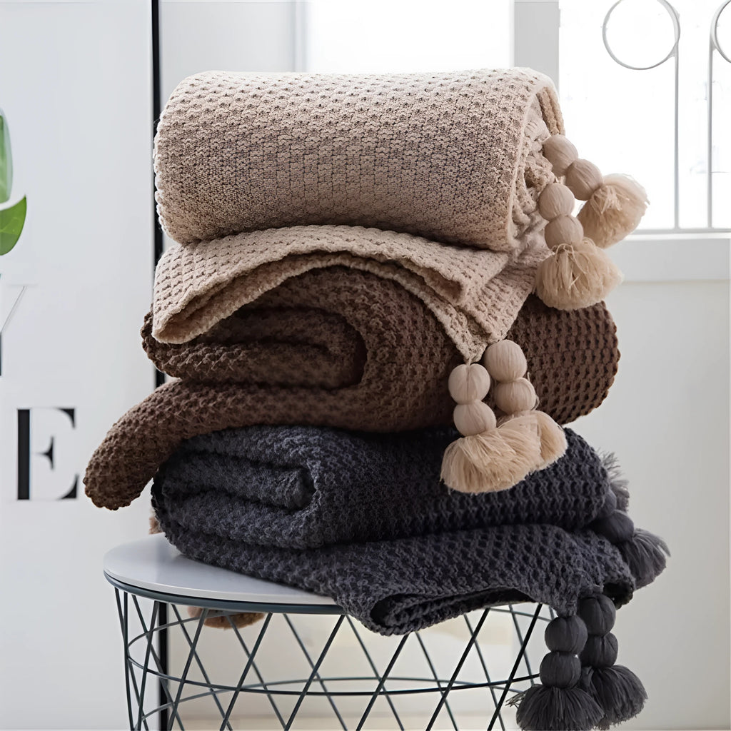 Nordic-style fringed knit acrylic blanket in a plain pattern, shown in a neutral colour on a sofa.